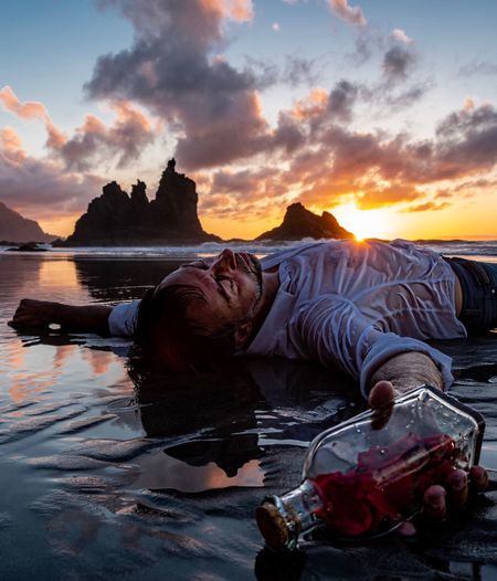 Man lying down against sky during sunset