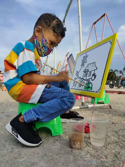 Full length of boy wearing mask paining on paper outdoors