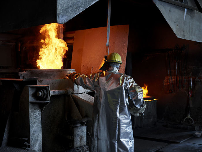 Foundry worker burning metal in furnace at workshop