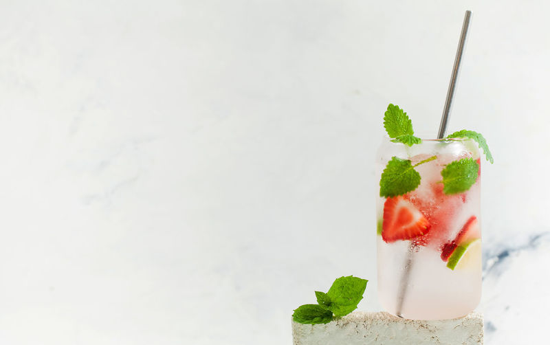 A refreshing summer drink with strawberries, lemon and mint in a glass on a light background. 