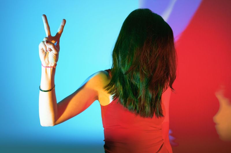 Woman gesturing peace sign against blue background