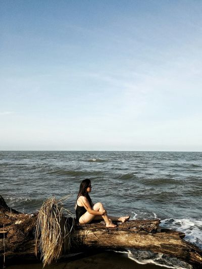 Man sitting on shore against sea against clear sky