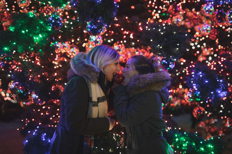 Female friends eating caramelized apple during christmas at night