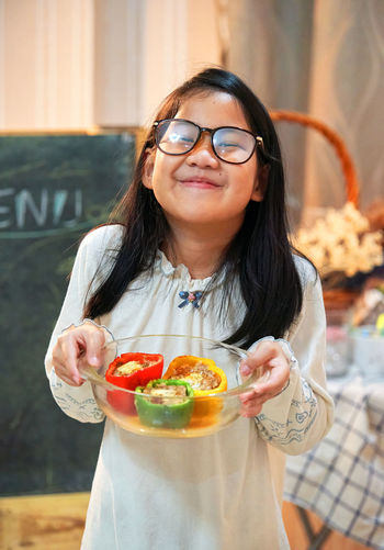 Portrait of smiling girl holding bell peppers in bowl at restaurant