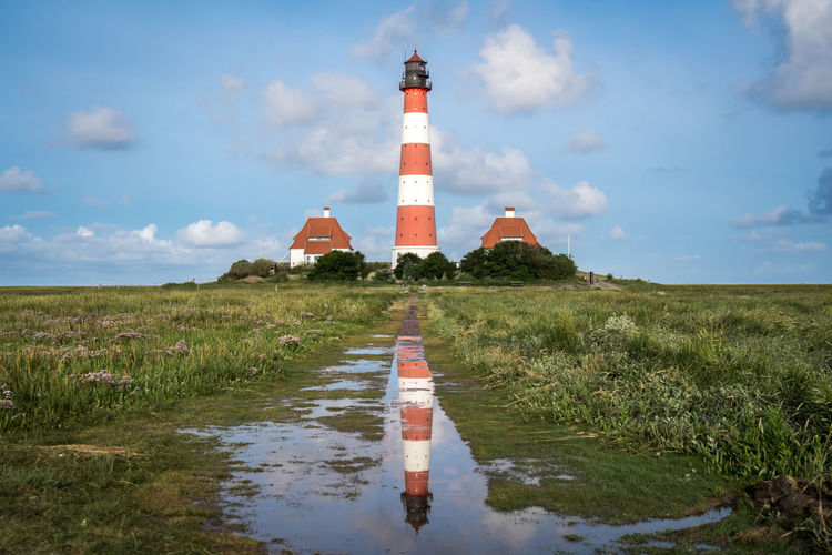 Lighthouse amidst field and building against sky