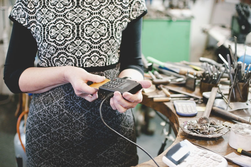 Midsection of senior craftsperson using credit card reader in jewelry workshop