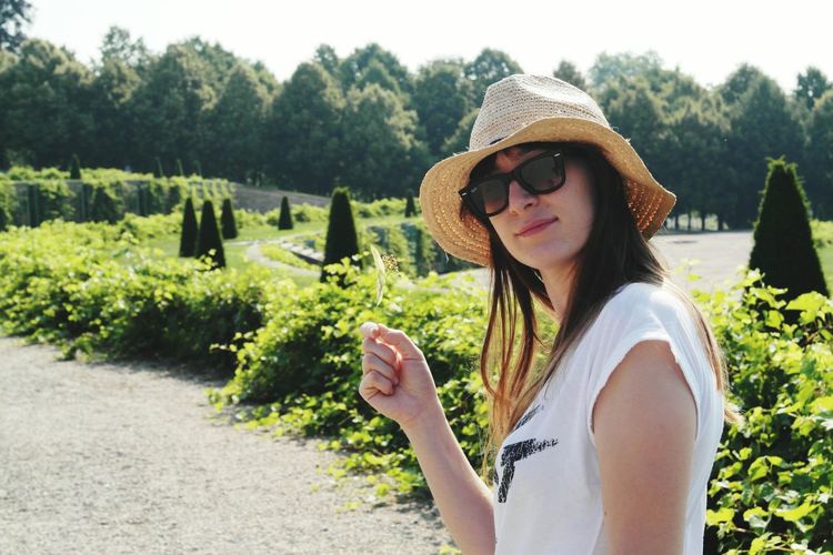 Portrait of beautiful woman wearing sunglasses and hat while standing in garden