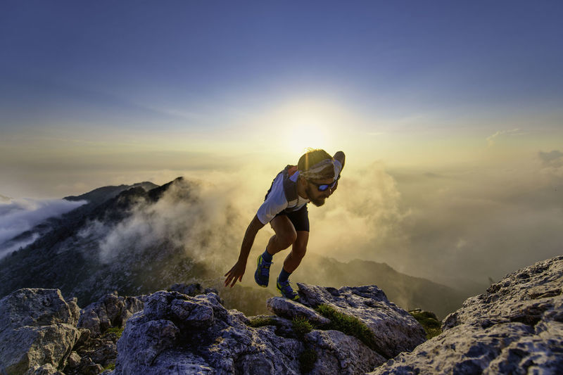Sky runner man uphill on rocks at sunset