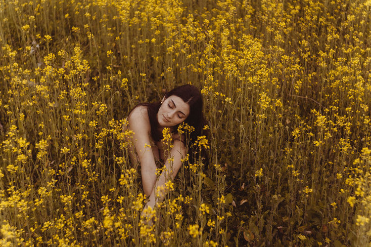 High angle view of young woman in bikini with eyes closed sitting amidst flowers on field