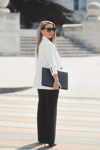 Woman wearing sunglasses standing against wall in city