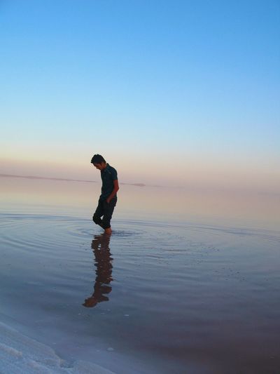 Young man walking in sea against clear sky during sunset