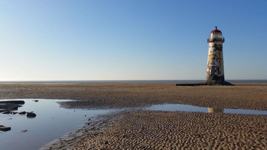 Lighthouse at beach against clear sky