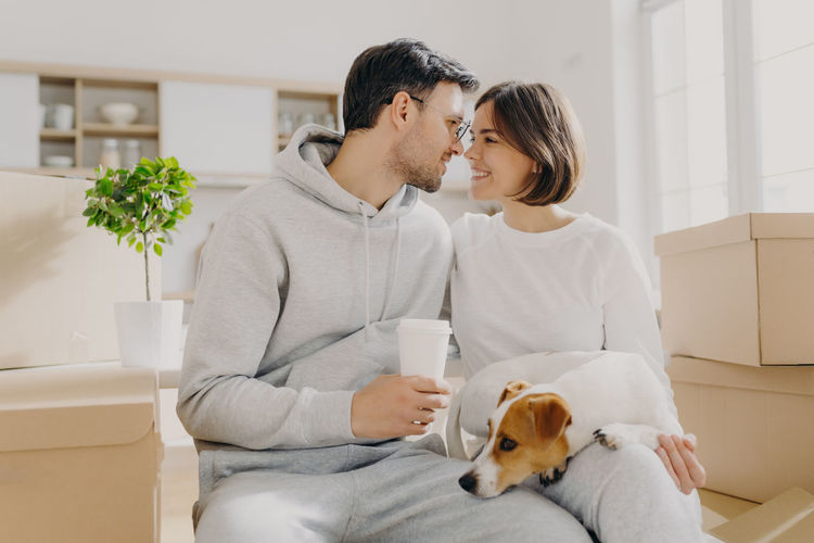 Romantic couple with dog sitting amidst boxes in new house