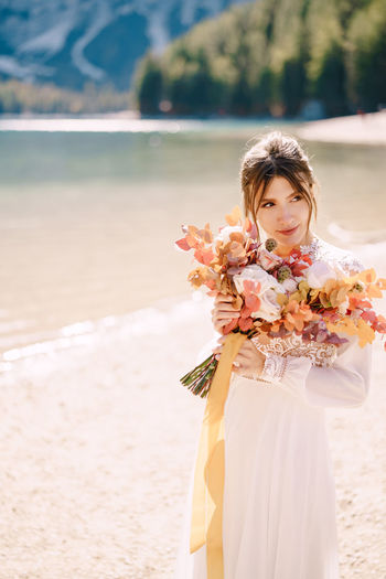 Bride holding bouquet looking away by riverbank