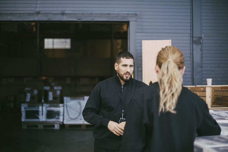 Male entrepreneur discussing with female colleague outside distribution warehouse