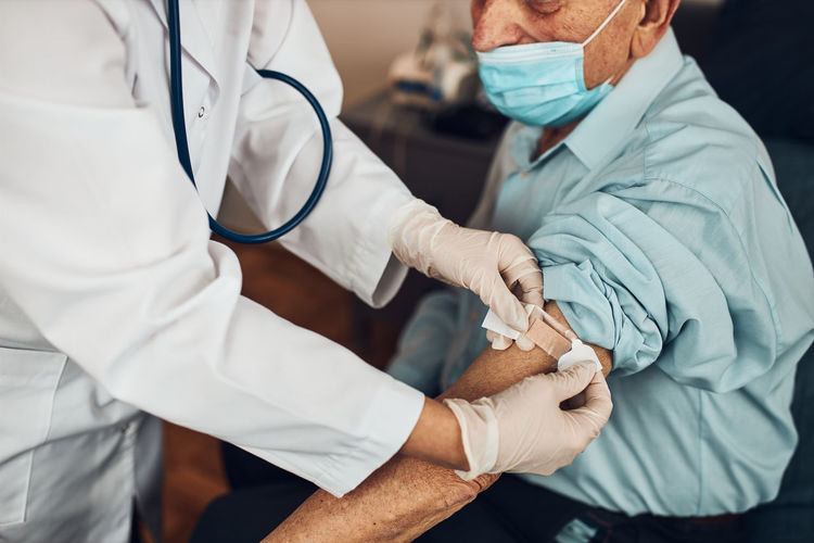 Doctor putting a plaster in place of injection of vaccine to senior man patient. covid-19