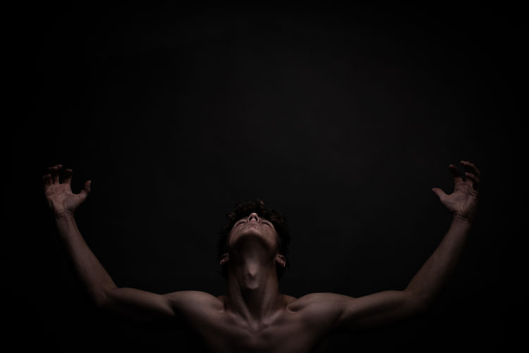 Portrait of shirtless man against black background looking in the sky to the light
