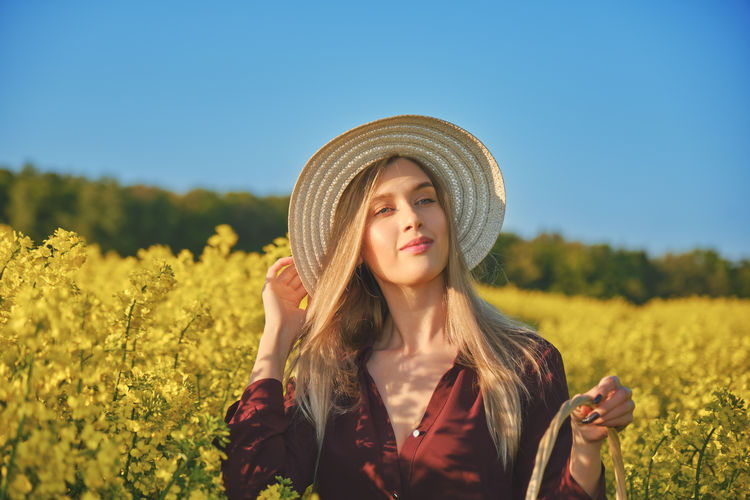 Happy young attractive woman in hat and purple dress on rapeseed field