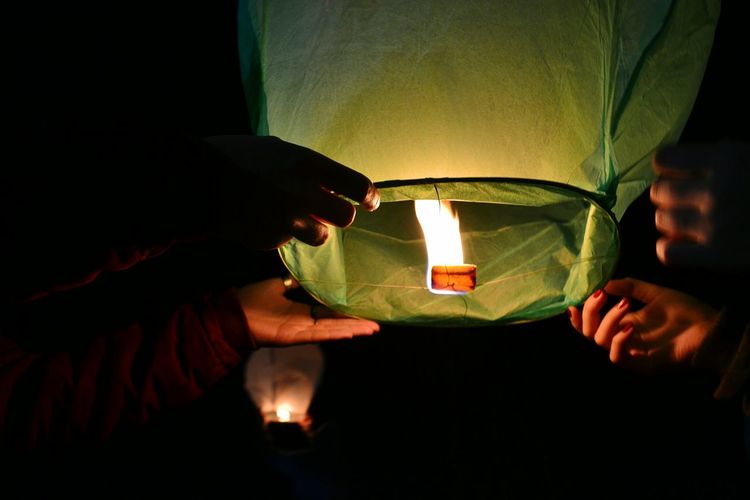 Cropped hands holding paper lantern at night