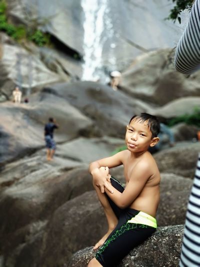 Portrait shirtless boy sitting on rock