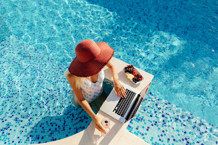 Directly above shot of woman wearing hat using laptop by swimming pool