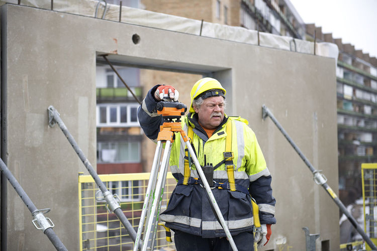  senior surveyor worker working with theodolite or tacheometer transit equipment at construction site 