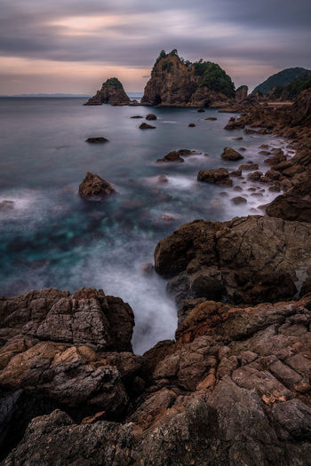 Scenic view of rocks beach against cloudy sky during sunset