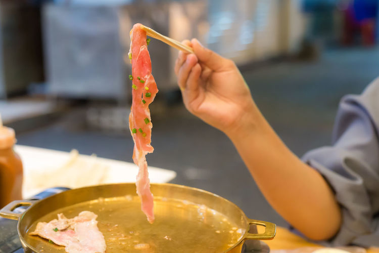 Close-up of woman hand holding meat with chopsticks