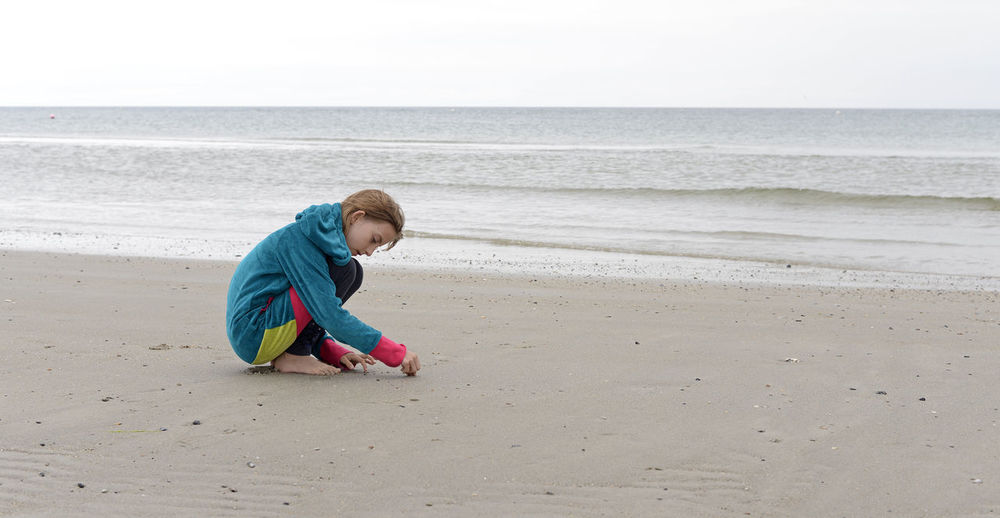 Profile view of girl crouching at beach