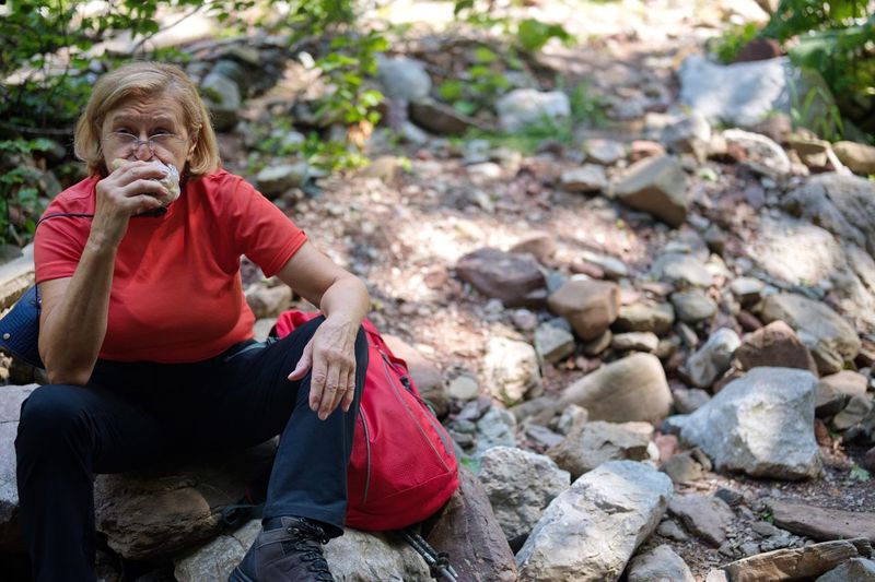 Senior woman sitting on the rock in nature and eating sandwich