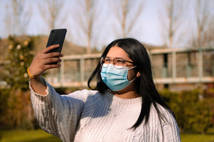 Woman with a surgical mask using the mobile in social networks. woman in the park.