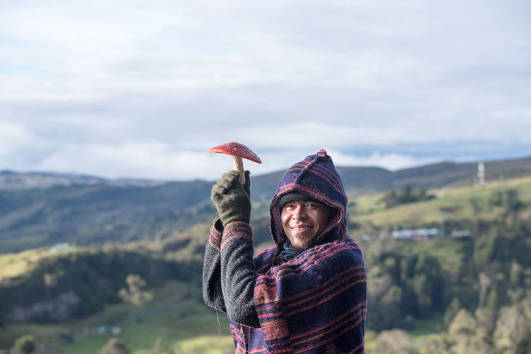 Colombian native american man in traditional clothing with mushroom as umbrella against panorama