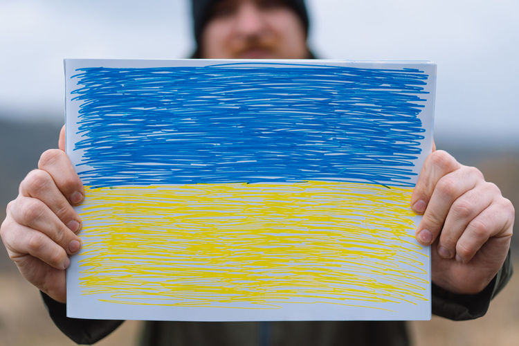 Cropped hands of woman holding multi colored pencils against sky