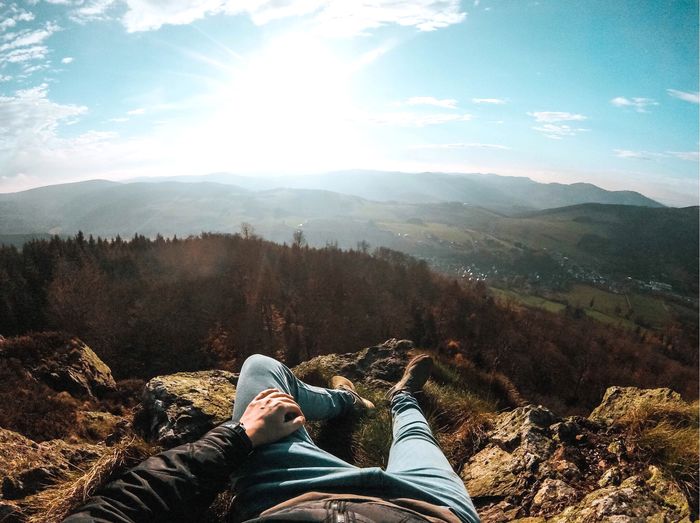 Low section of man relaxing on mountain against sky