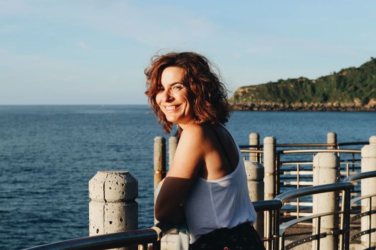 Smiling woman sitting by sea against sky