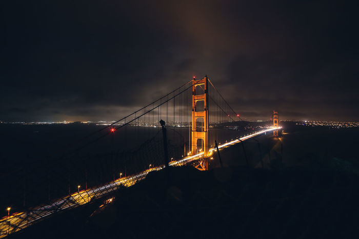 Illuminated suspension bridge over sea against sky at night
