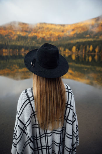 Young blonde woman wearing poncho and hat near the autumn forest. wanderlust,travel concept.