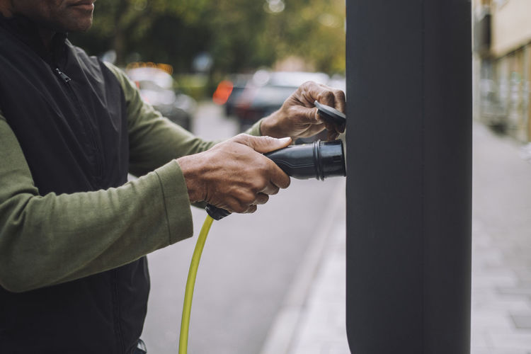 Man removing charger plug from kiosk at car charging station