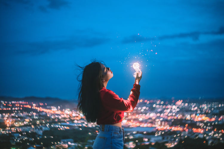 Woman with illuminated light bulb standing in city at night