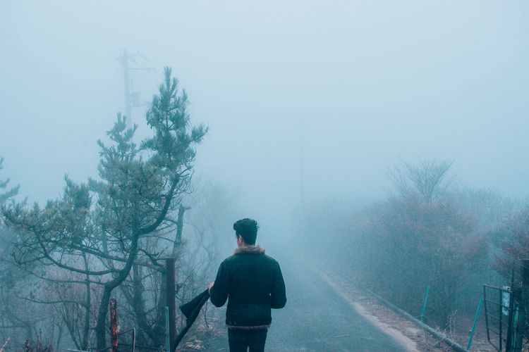 Rear view of man standing on road during foggy weather