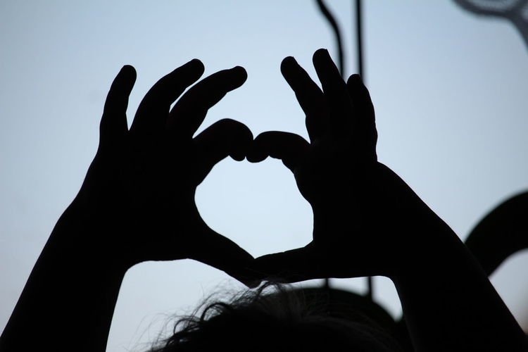Silhouette hand holding heart shape against sky