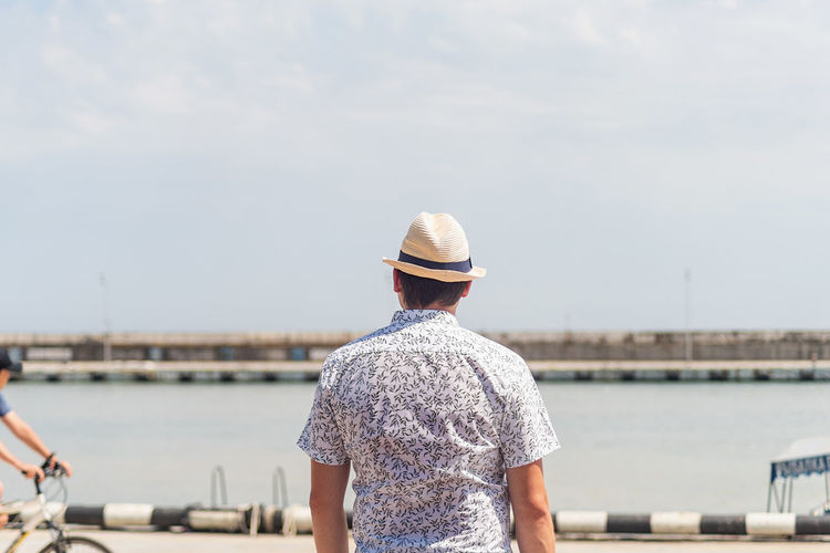 Summer travel. back view of a man in shirt and summer hat looking at the sea, standing 