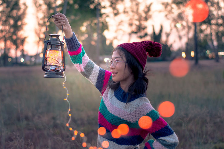Side view of woman holding illuminated lights in lantern during winter