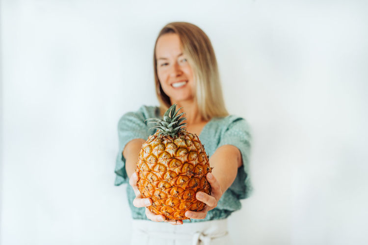 Young blond woman holding azorean pineapple in front of her