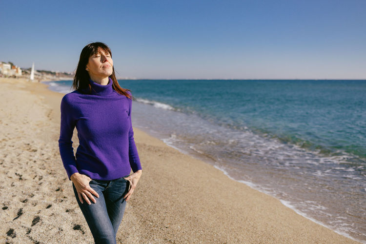 Beautiful mature woman relaxing breathing fresh air on a sunny winter day at the beach