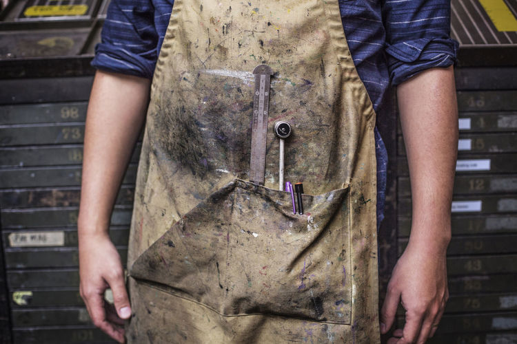 Midsection of man with apron standing in workshop