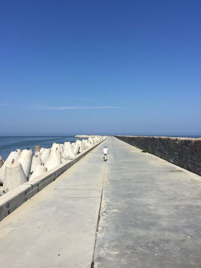 Empty footpath by sea against clear blue sky