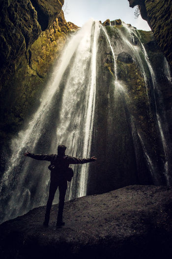 Rear view of man standing on rock against waterfall