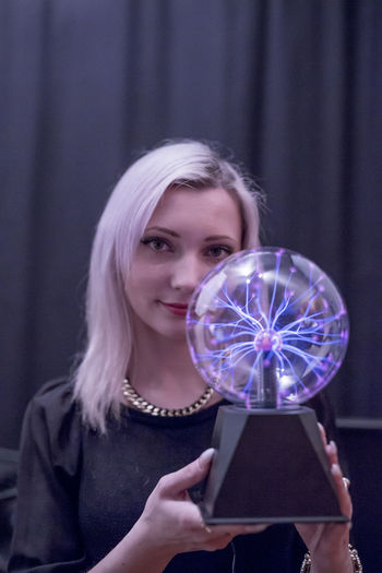 Close-up portrait of young woman holding plasma ball over black background
