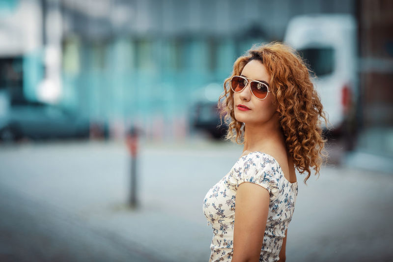 Young moroccan woman with curly hair, wearing sunglasses, turning to camera, in urban environment 